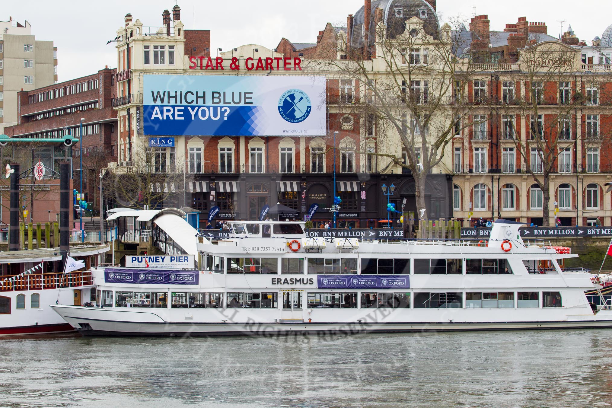 The Boat Race 2013: "Which Blue are you"-billboard by Boat Race sponsor BNY Mellon ouside the Star & Garter River Bar & Eaterty at Putney Embankment. In the foreground Putney Pier, seen from Fulham Palace Gardens on the other side of the River Thames..
Putney,
London SW15,

United Kingdom,
on 31 March 2013 at 11:45, image #33