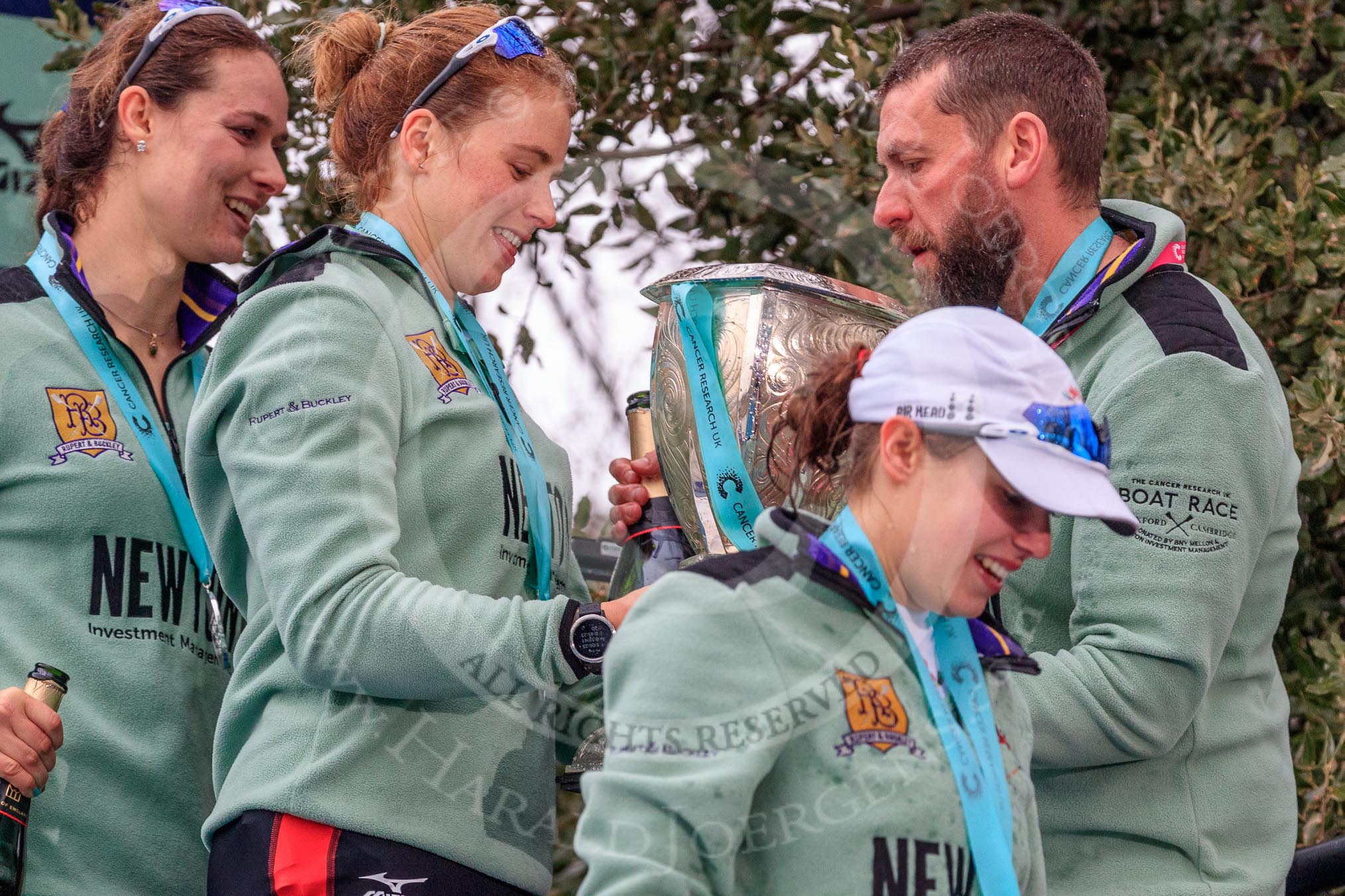 The Cancer Research UK Women's Boat Race 2018: Thea Zabell, Alice White, and Sophie Shapter leaving the podium, all still wet after spraying lots of Castle Down Brut. On the right, with the Boat Race trophy, Vambridge Head coach Rob Baker.
River Thames between Putney Bridge and Mortlake,
London SW15,

United Kingdom,
on 24 March 2018 at 17:10, image #303