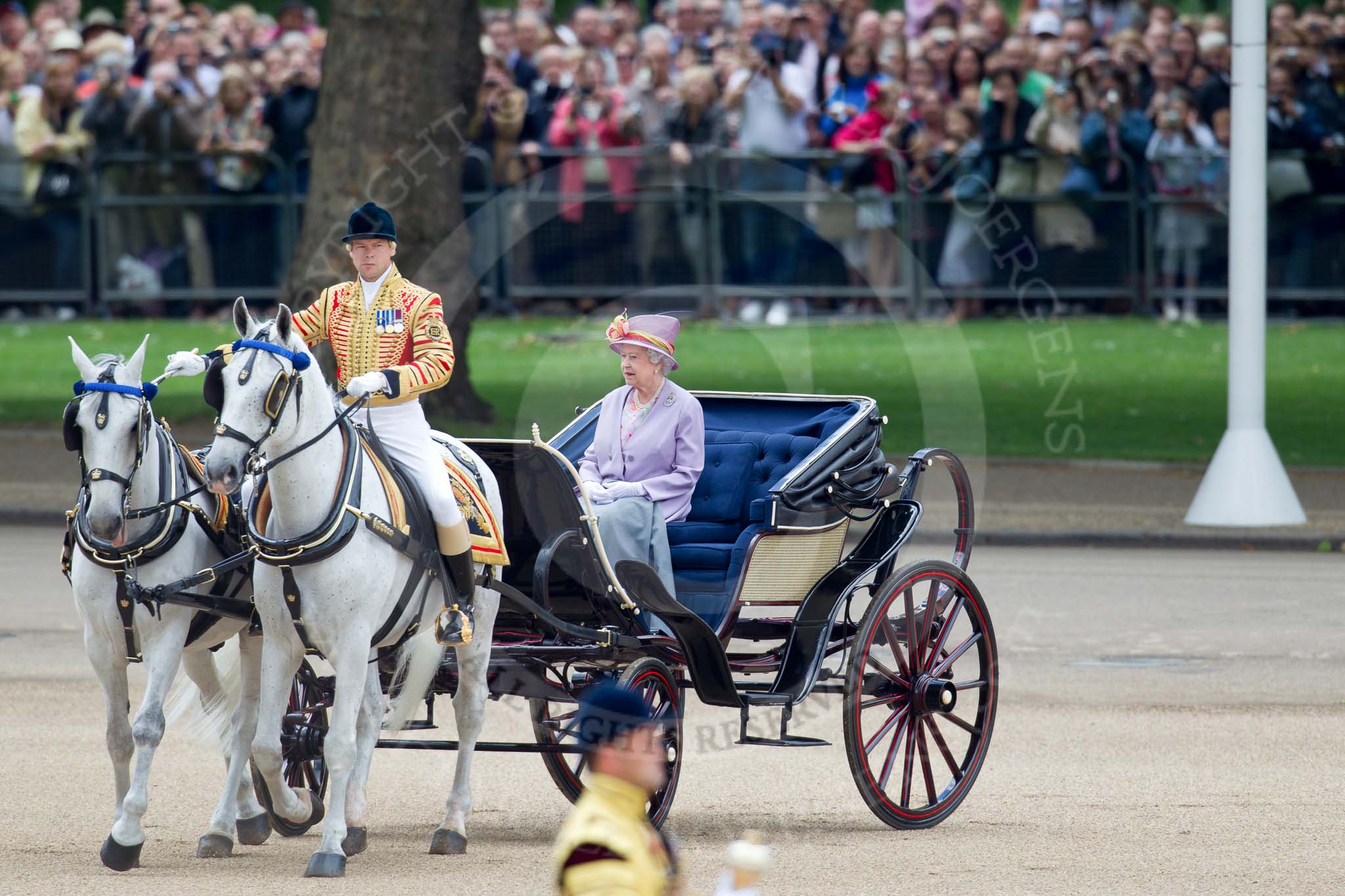 Trooping the Colour 2010: Her Majesty The Queen, sitting in her Ivory Mounted Phaeton,  inspecting the line of soldiers on the parade ground.

In the background spectators watching from St. James's Park, on the western end of the parade ground, and in the foreground one of the Drum Majors..
Horse Guards Parade, Westminster,
London SW1,
Greater London,
United Kingdom,
on 12 June 2010 at 11:06, image #88