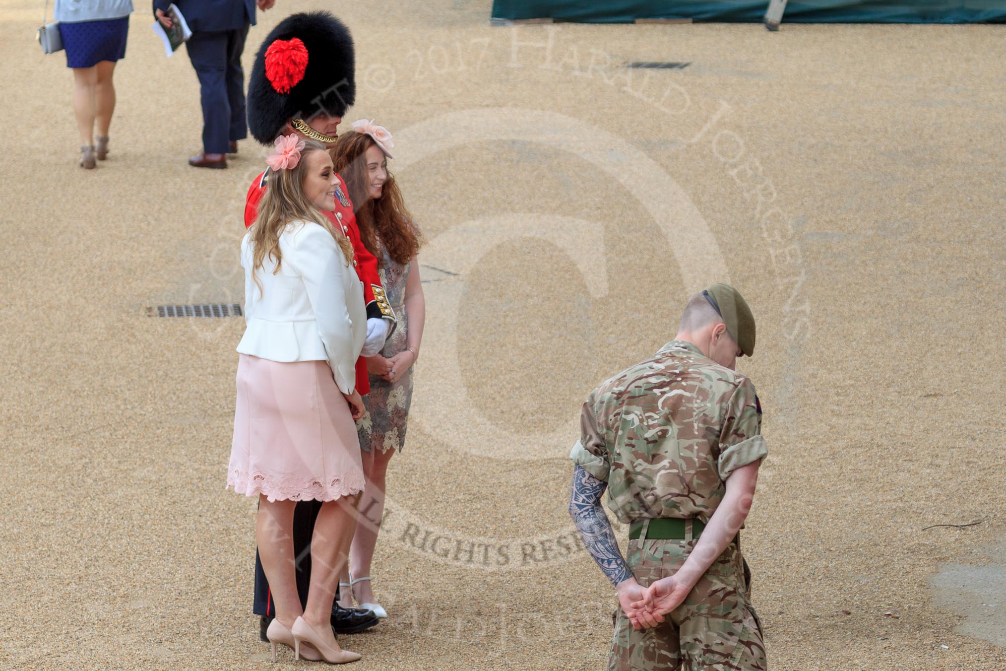 Two young ladies, wearing fascinators, posing with Coldstream Guards officer for a photo before Trooping the Colour 2018, The Queen's Birthday Parade at Horse Guards Parade, Westminster, London, 9 June 2018, 09:02.