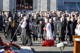 Following the Forces Chaplain and the Bishop of London, Cross Bearer, the 10 Children of the Chapel Royal, and the 6 Gentlemen-in-Ordinary ares leaving Whitehall towards the Foreign- and Commonwealth Office building. In the Foreground the Eastern side of the Cenotaph with the wreaths of the Royal Family.